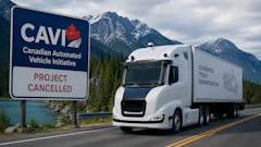 Autonomous truck driving past CAVI project cancelled sign with snow-capped mountains and lake in background