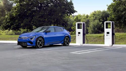 Blue electric vehicle charging at two white fast-charging stations in outdoor parking area with green trees