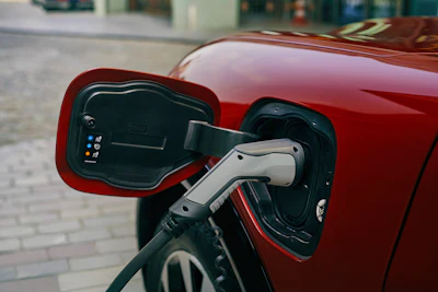 Electric vehicle charging port with white connector plugged into red car's charging inlet