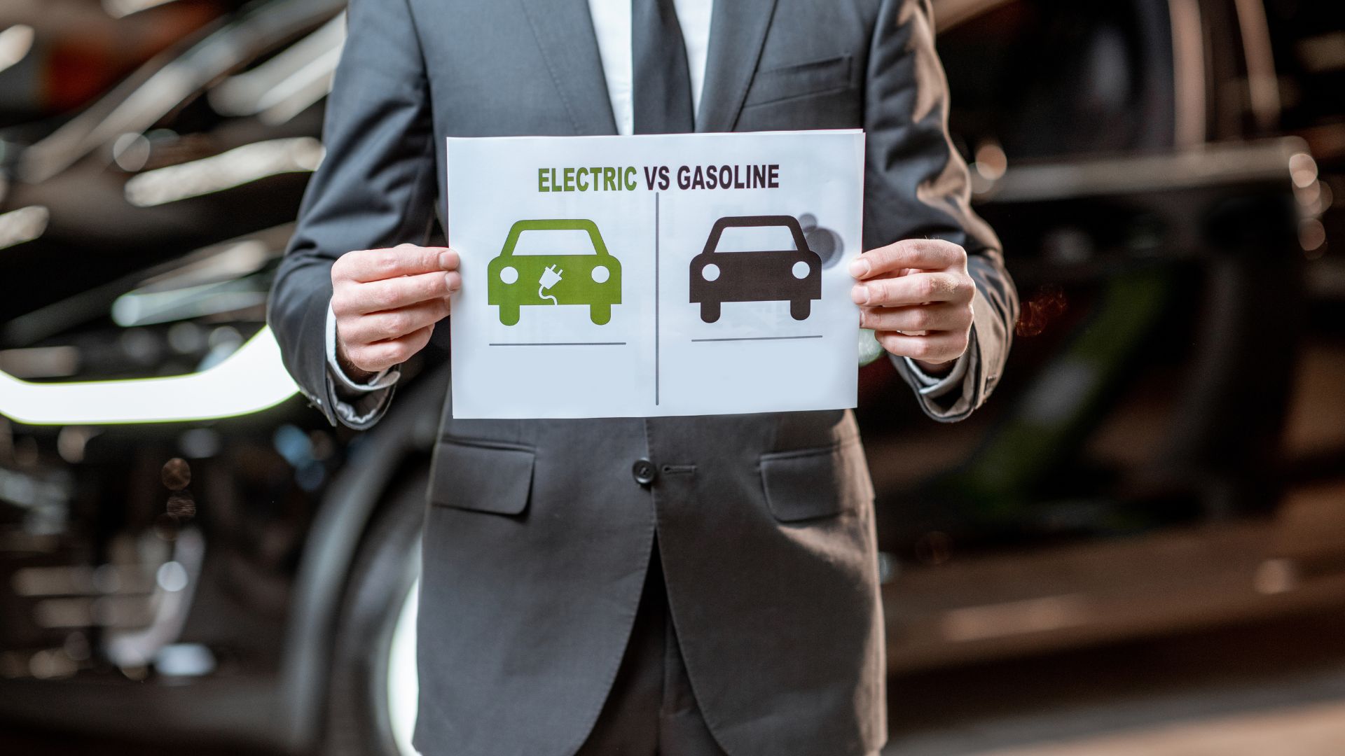 Businessman holding electric vs gasoline vehicle comparison chart in automotive workshop