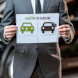 Businessman holding electric vs gasoline vehicle comparison chart in automotive workshop