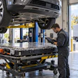 Technician inspecting electric vehicle battery pack on hydraulic lift in automotive service garage