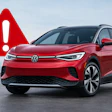 Red Volkswagen ID.Buzz electric SUV with warning alert symbol on gray surface