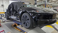 Black electric vehicle on service lift in factory workshop with open door and technician overhead