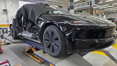 Black electric vehicle on service lift in factory workshop with open door and technician overhead