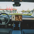 Tesla vehicle interior dashboard view with steering wheel and touchscreen display facing a shopping center parking lot
