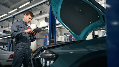 Automotive technician inspecting vehicle engine with tablet in professional garage workshop