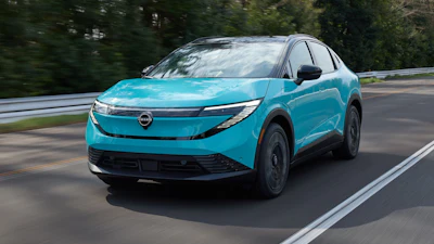 Turquoise Nissan Ariya electric SUV driving on a highway with trees in background